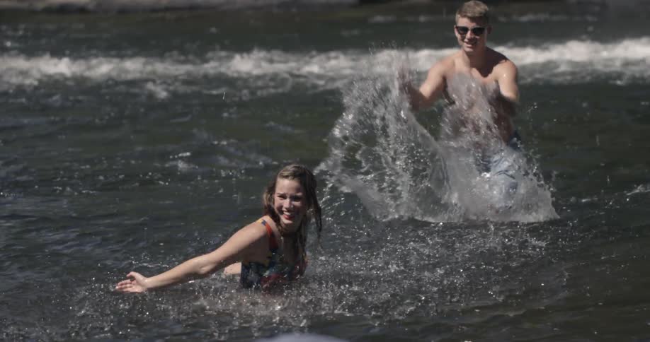 Guy splashing girl in a body of water and smiling