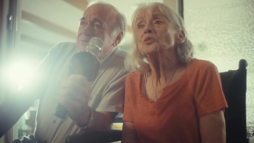 An elderly couple joyfully sings together into a microphone