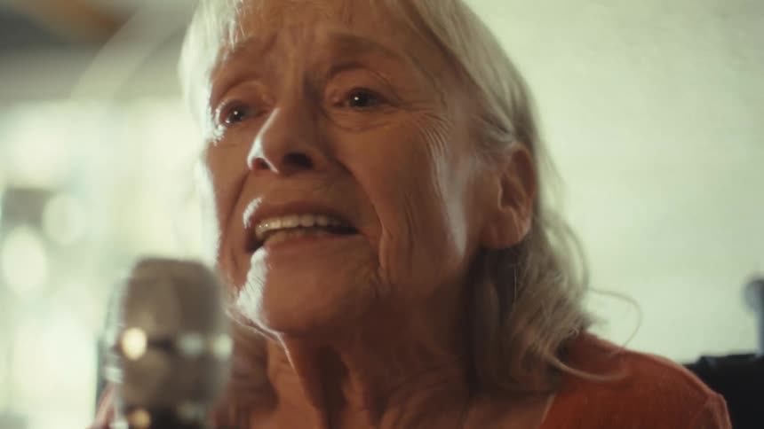 Elderly woman sings into a microphone with passion