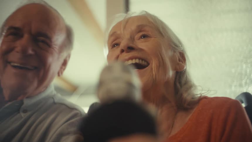 An elderly couple singing on a microphone in an indoor setting