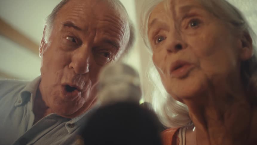 An older couple sings happily into a microphone