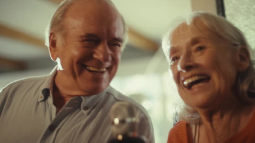An elderly couple happily sing into a microphone together at home
