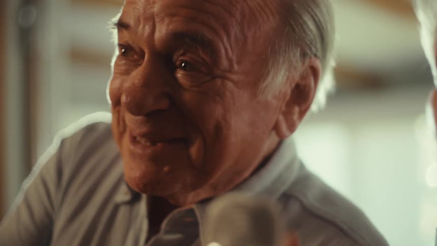 An older couple is laughing and singing together the man is holding a microphone and both have happy expressions on their faces the woman is wearing an orange shirt and the man is wearing a gray shirt