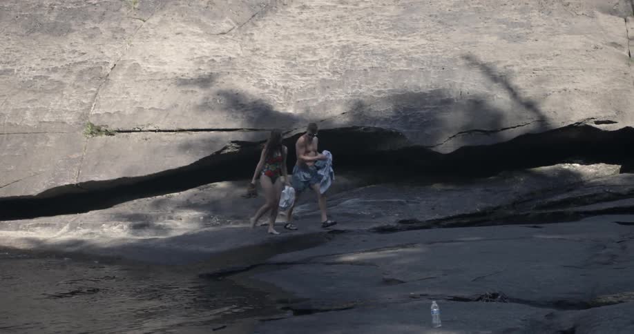 A couple walks over a large rock next to a body of water