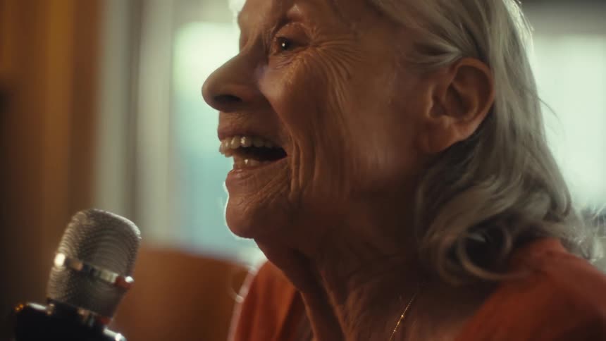 An elderly female sings loudly into a microphone seeming joyful