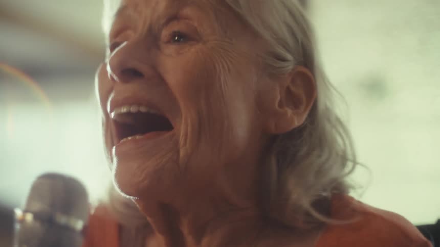 Elderly woman smiles while singing joyfully into a microphone