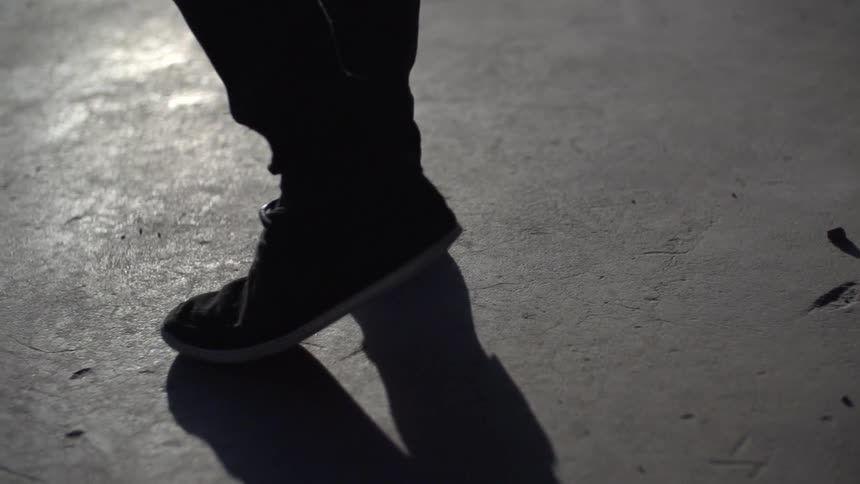 Close shot of someone's feet and calves as they walk along concrete, stop, turn around and walk back the other way