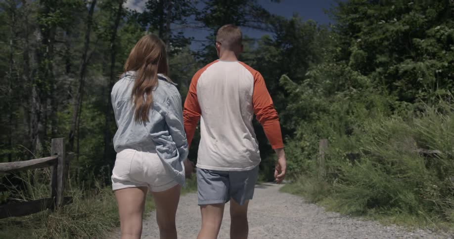A man and woman hold hands walking on a sunny day