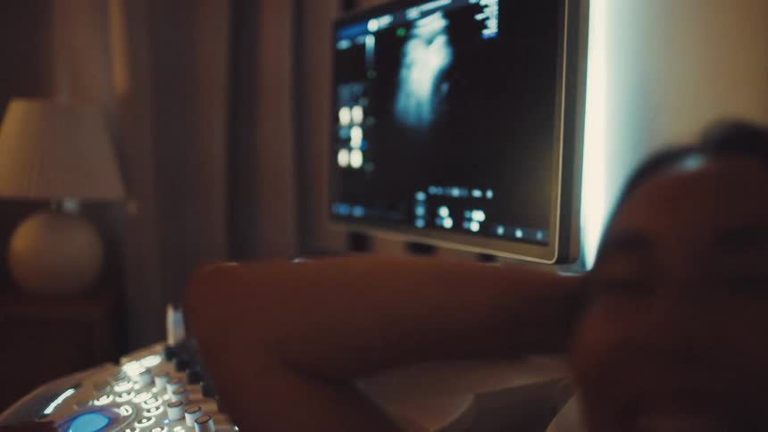 A woman in a room with a monitor and medical equipment looks at a screen and then looks up with a smile and a laugh