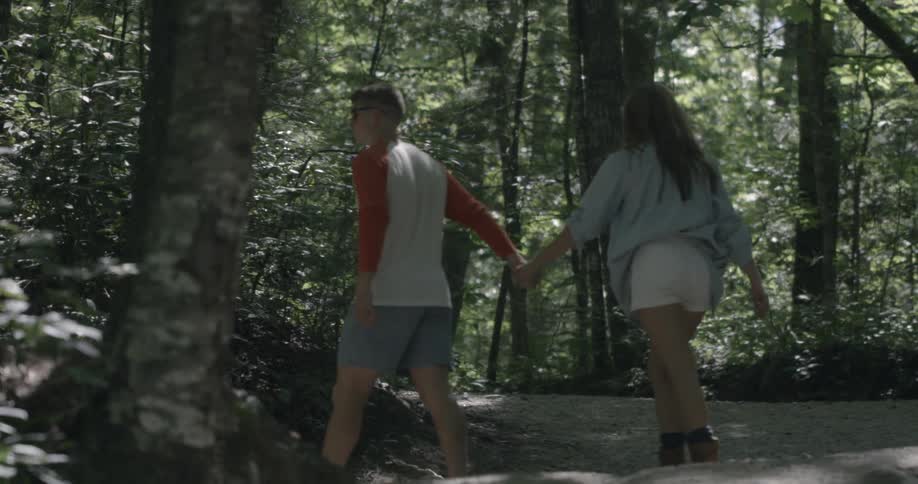 A couple walk uphill towards the forest on a sunny day