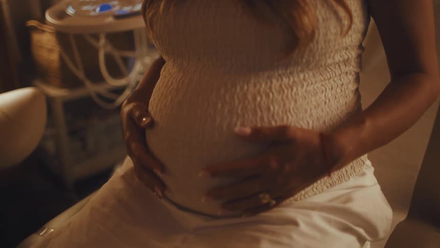 Pregnant woman gently caresses her belly with both hands in a caring gesture