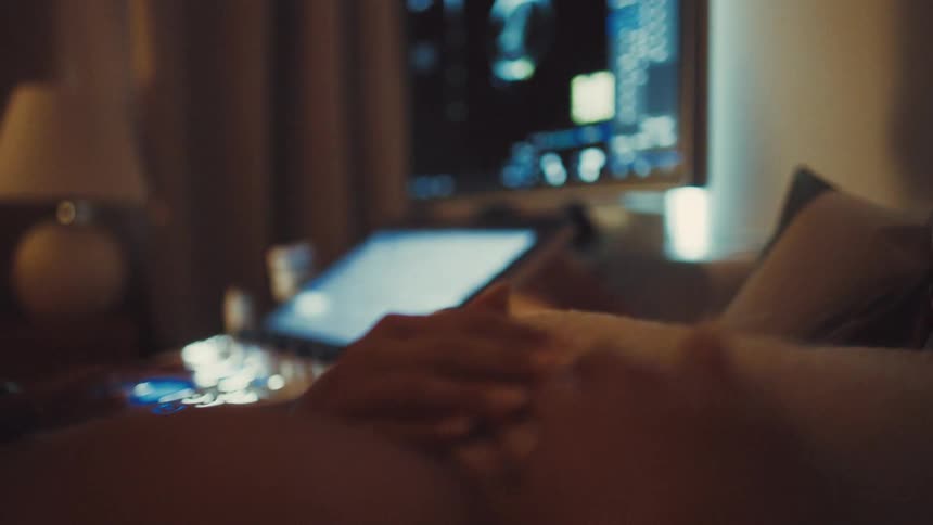 A pregnant woman with a large baby bump lies on a hospital bed her tummy exposed as a nurse performs an ultrasound