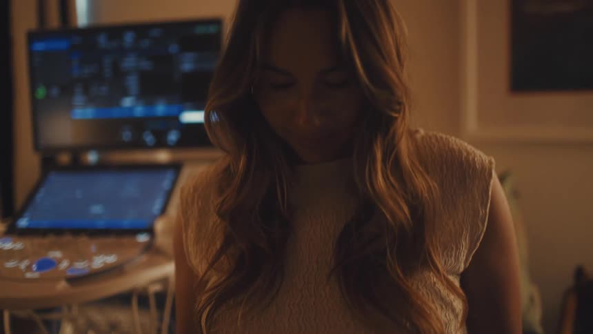 In a warmly lit medical examination room a pregnant woman lovingly holds her belly and looks down with a gentle expression with an ultrasound machine visible in the background