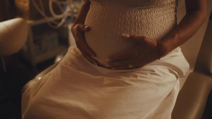 Pregnant woman sitting caresses her belly with both hands
