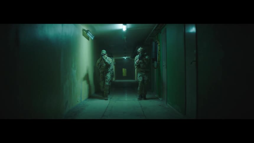 The footage shows a dark empty hallway in what appears to be a building or facility two people in militarystyle gear and carrying rifles enter the hallway then cautiously move forward as if they are on a mission