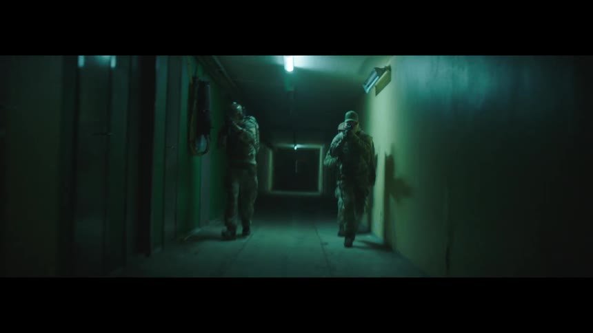Three people in military gear walk down a hallway with their rifles