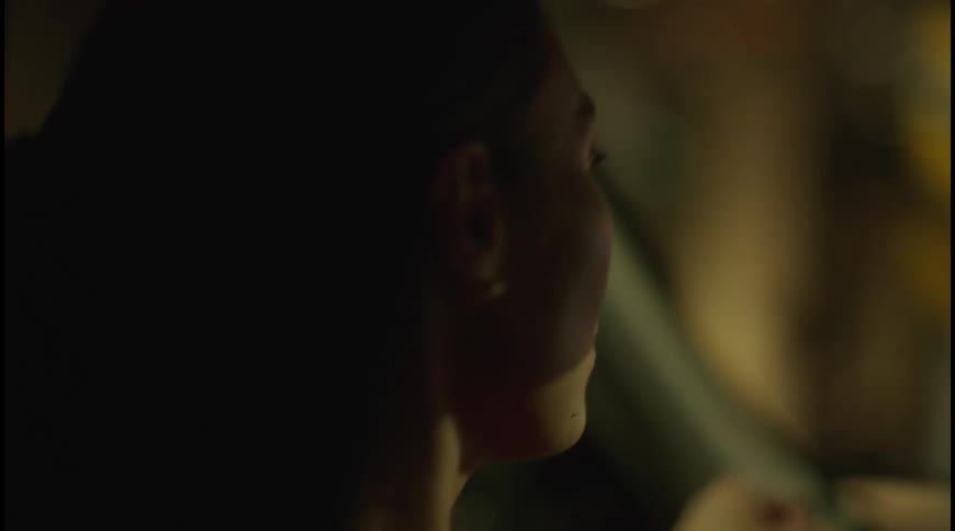 A woman with her hair pulled back is sitting in the drivers seat of a car at night her face is in a soft profile illuminated by the muted lights of the city outside the window