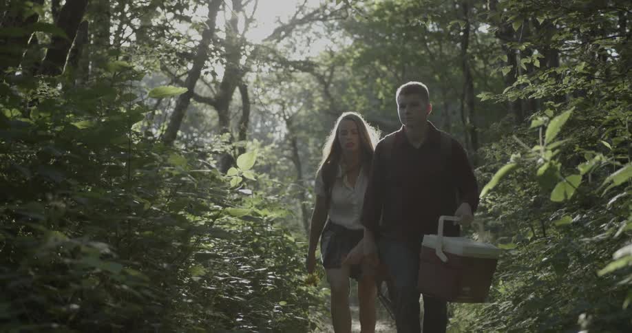 A man and woman walk along a trail with camping equipment