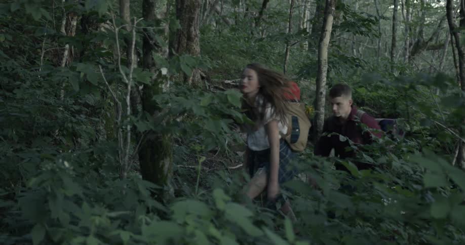 Man and woman hike through the woods carrying backpacks