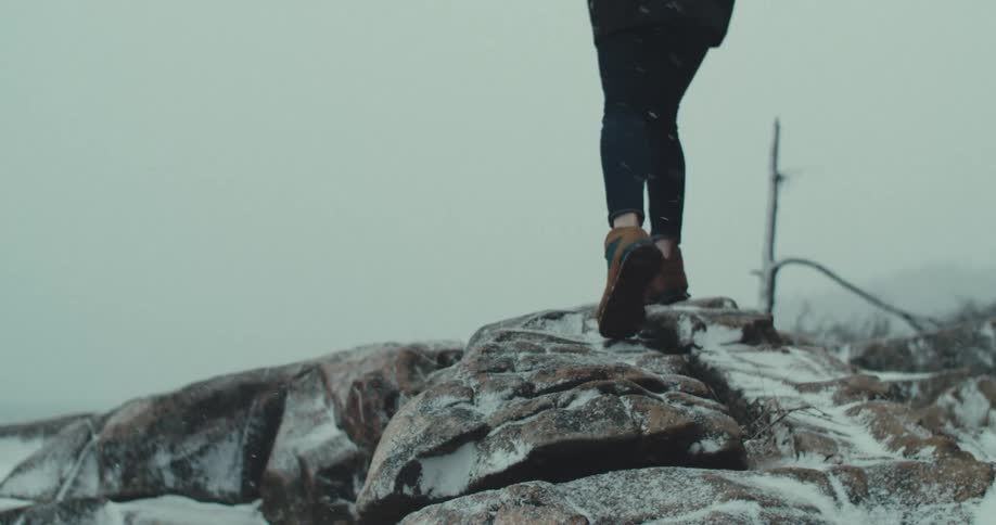 The woman walks over the rocks as it snows