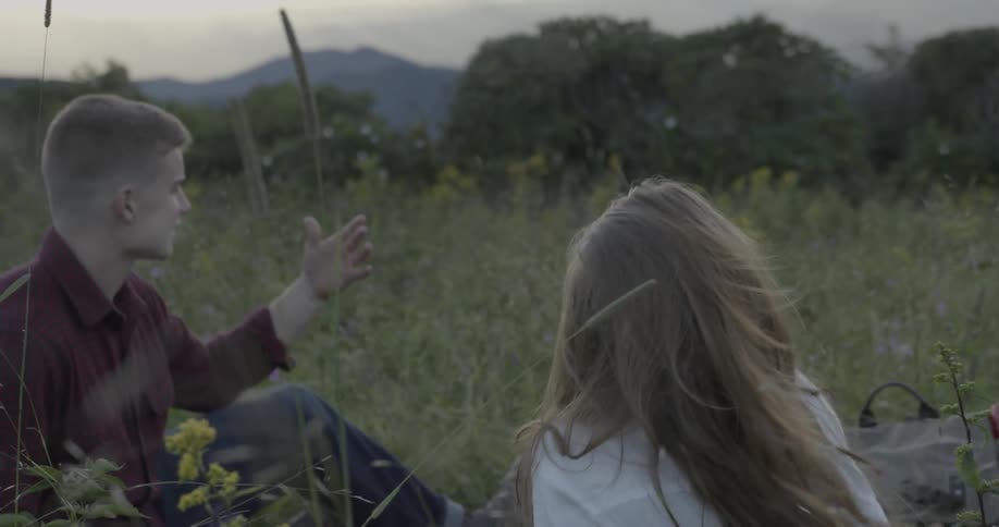 A man and woman sit and laugh in a field