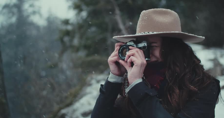 Woman in a beige hat takes a photograph in the snow with a focused expression