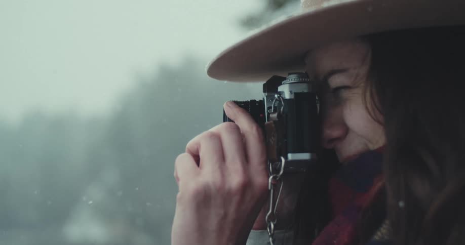Woman in the snow outdoors by a lake handling a camera