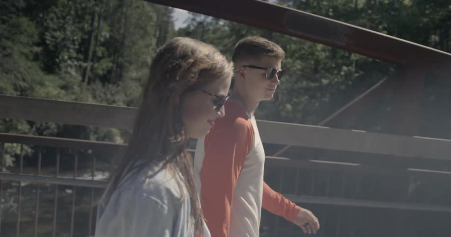 A man and woman walk across a bridge together on a sunny day