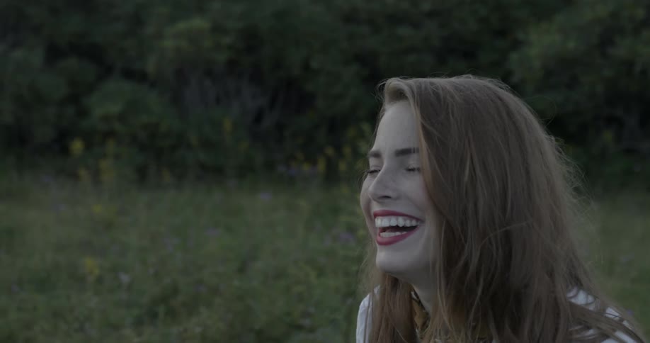 Woman laughs as she stands in a tree lined field
