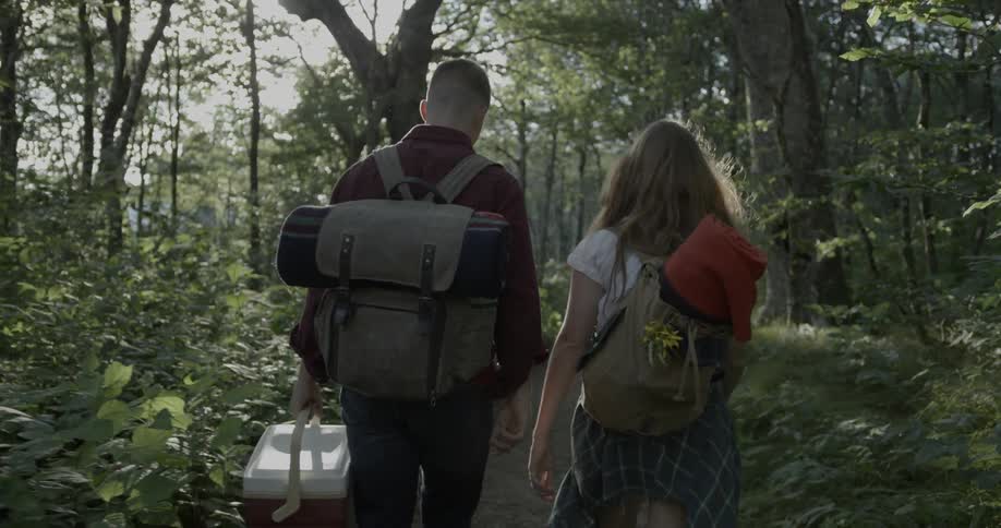 A man and woman walk in the woods with camping equipment