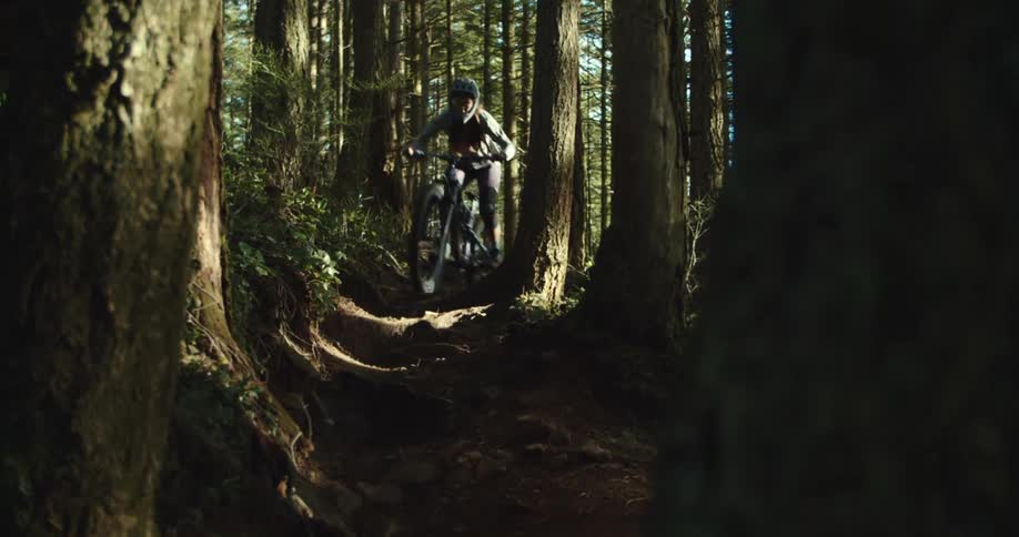 A person on a bike rides down a trail in a forest towards the camera