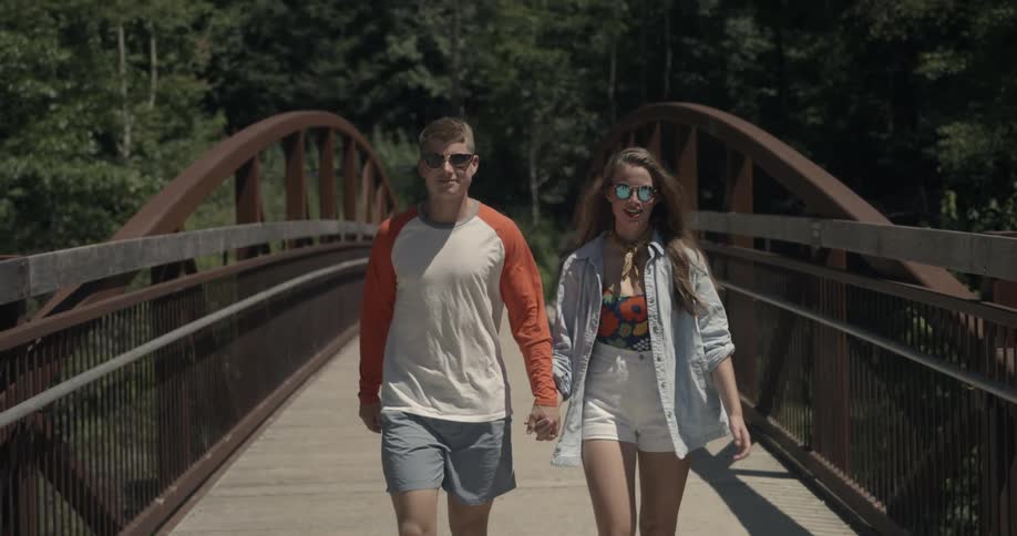 Two teenagers hold hands as they walk over a bridge