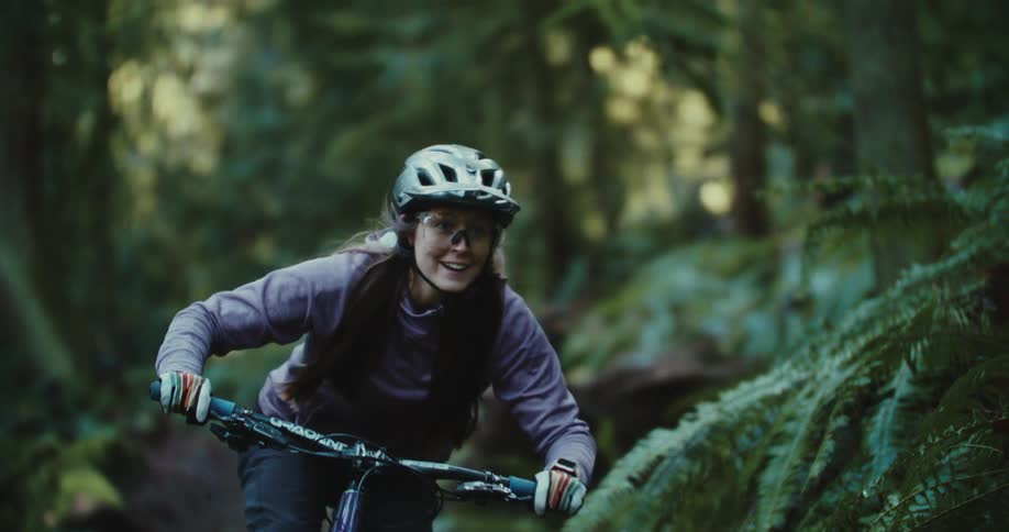 A young girl rides a bike on a trail in a forest with green plants