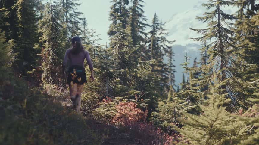 Woman running on a mountain trail surrounded by trees