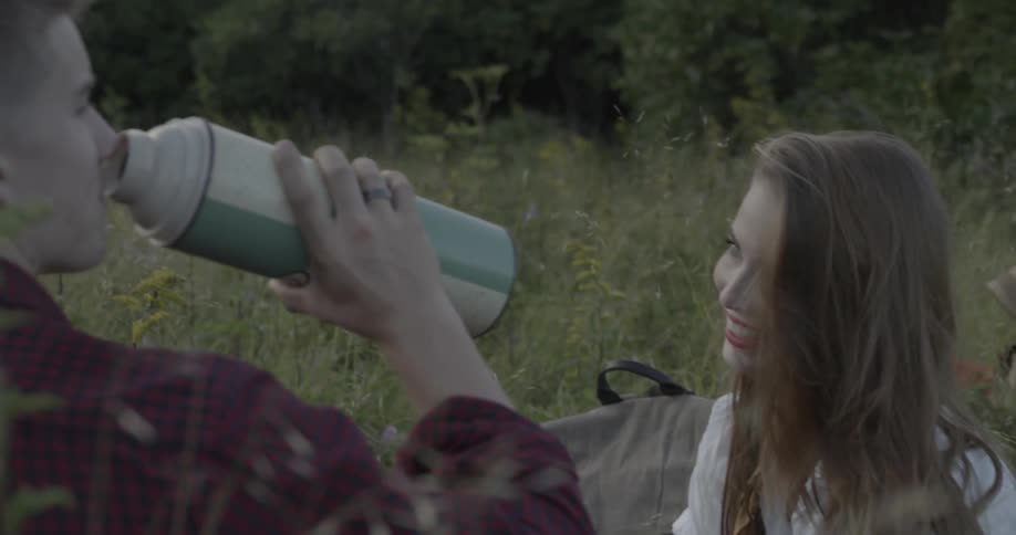 A man pours something from a thermos then takes a drink