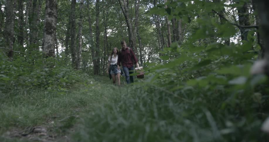 Man and woman walking in forest with cooler in breezy day