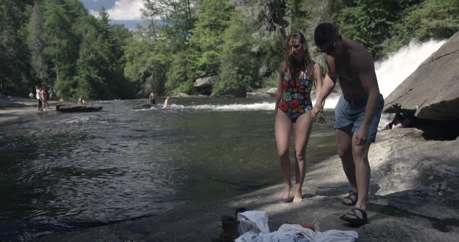 A man and woman hold hands walking along the water