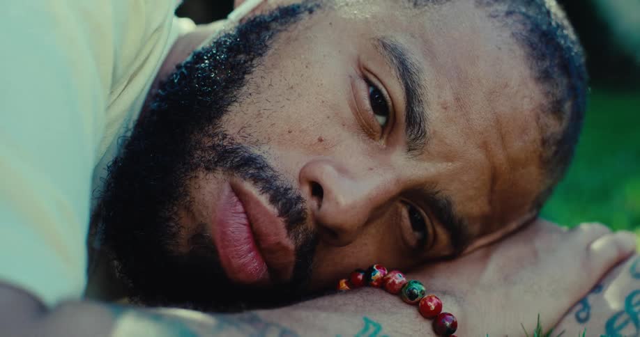 A person lies on the ground with their head resting on their arm and looks at the camera