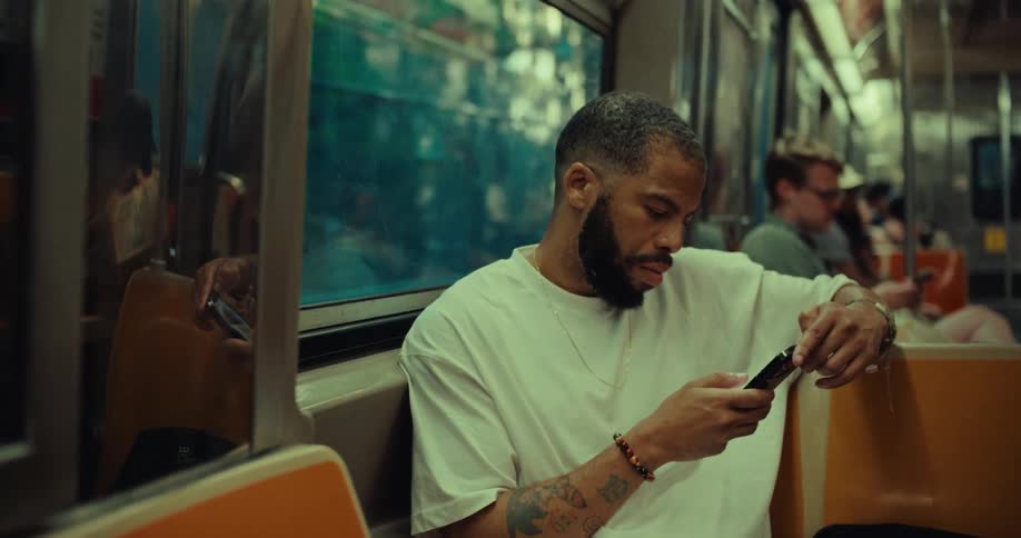 A man sits on a moving subway train looking at his phone