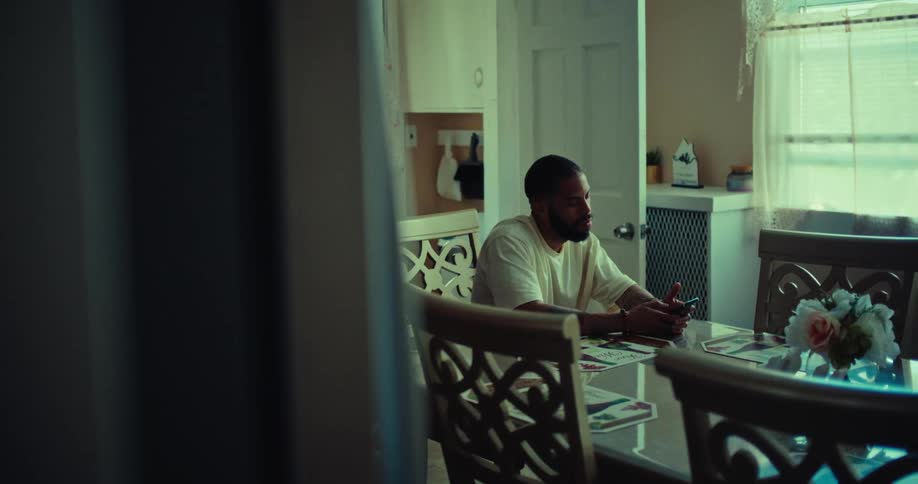 A man sits at a dining table making a phone call indoors