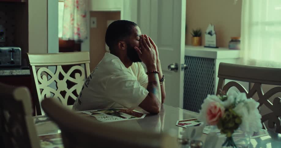 A man sits alone at a dining table looking out the window in deep thoughts