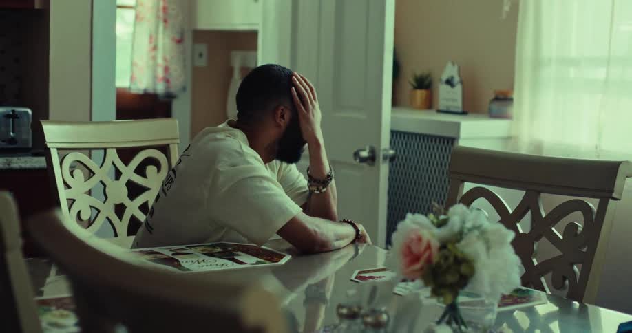The man is rubbing his face at the dining table