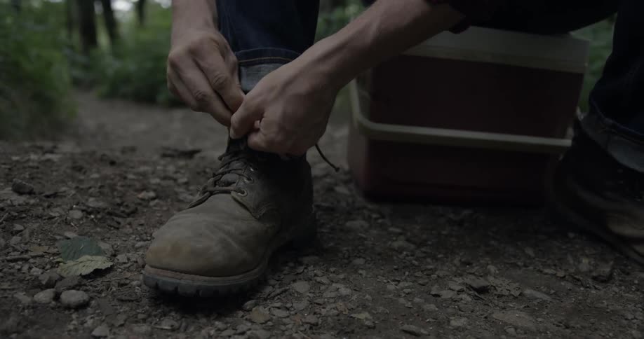 A man is tying his boots sitting on a cooler