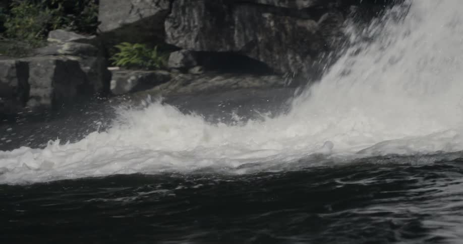 Water falls down into a river as people swim