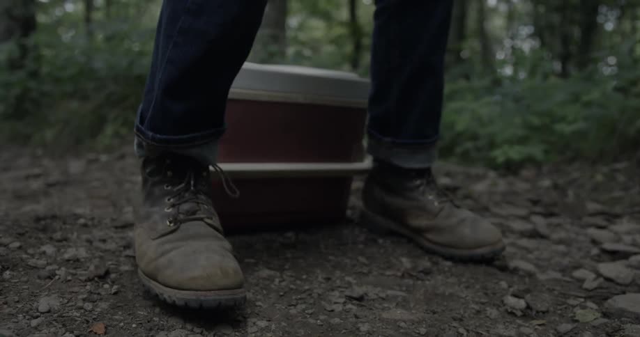 A man gets up from sitting on a cooler in the woods