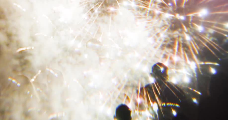 A crowd of people watching bright fireworks explode in the night sky