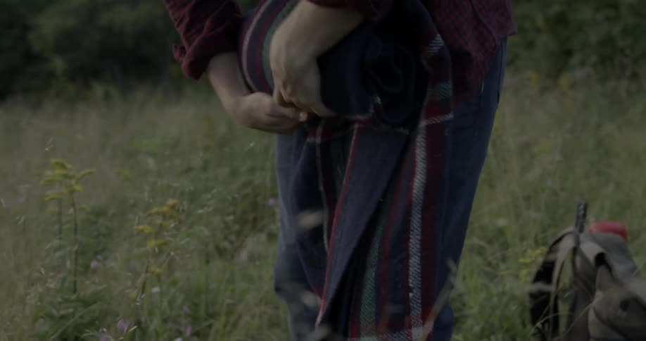 A man is rolling up a picnic blanket