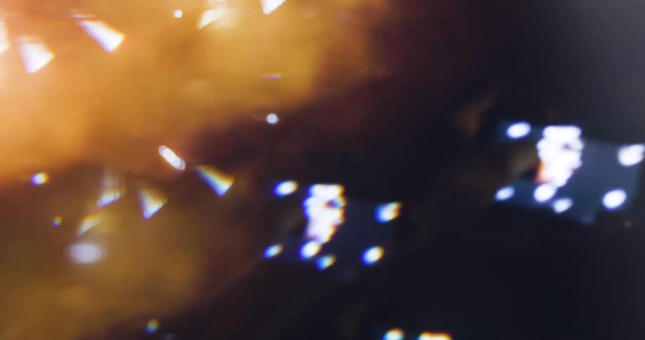 The first line of the video shows a burst of bright white and gold sparks against a dark background creating a glowing celebratory effect the second line focuses on a glowing orange and yellow background with large outoffocus white and golden light