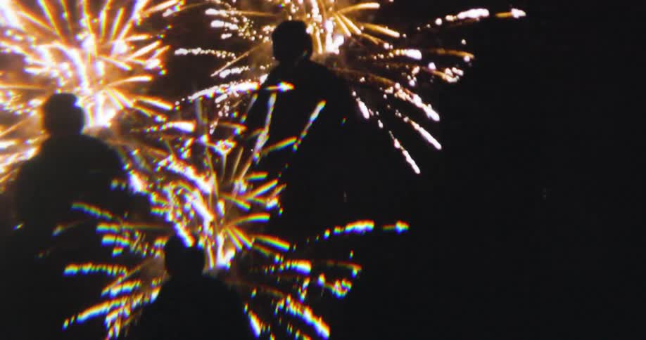 Silhouettes watch golden fireworks exploding in the night sky