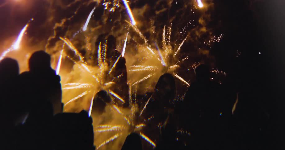The fireworks explode around the crowd at night